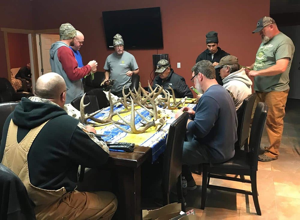 Men around a table measuring horns.